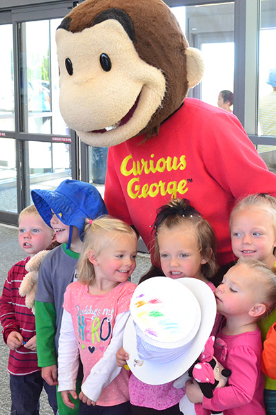 Person dressed as Curious George surrounded by children
